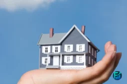 A hand holding a miniature house symbolizing the estate market