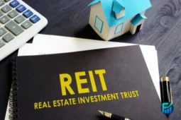 Notebook labeled “REIT” beside a small model house, representing investing in real estate investment trusts