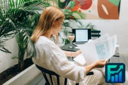 Woman analysing printed documents in a tropical workspace with laptop and drink, illustrating a focused annual financial review process.