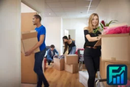Group of young adults moving boxes into an apartment, representing shared housing and co-living arrangements.