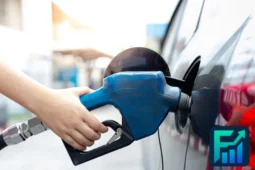 Hand holding a blue gas pump nozzle while refueling a car, illustrating the impact of fluctuating gas prices on everyday expenses.