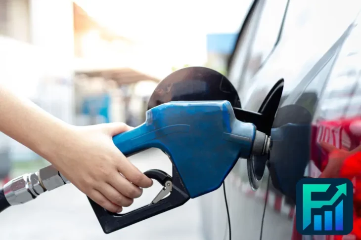 Hand holding a blue gas pump nozzle while refueling a car, illustrating the impact of fluctuating gas prices on everyday expenses.