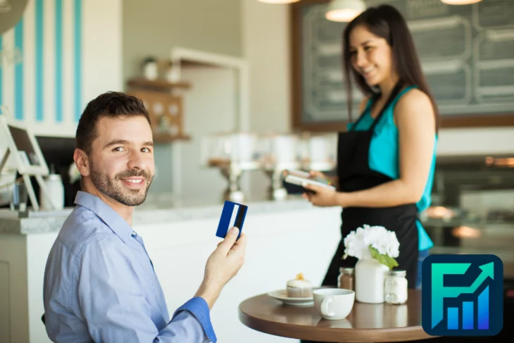 Man in a café smiles while tapping his card to earn Credit Card Rewards, server and pastry in view.