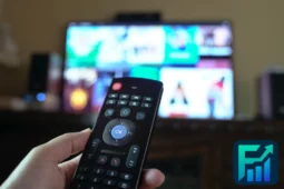 Hand holding a remote in front of a TV with multiple paid services on screen