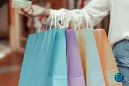 A person holding colorful shopping bags and a credit card, symbolizing impulse buying and unplanned spending habits.