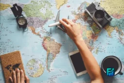 Paying for trips: hands hold a credit card and small plane over a world map with a camera, compass, phone and coffee nearby
