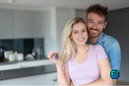 Young couple smiling and holding a house key, representing housing affordability in Canada.