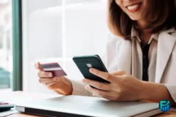 Woman smiling while using her phone and holding a credit card, representing online management of Credit Card Debt.