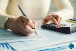 Person completing tax forms with a pen and calculator on a desk, representing the process of filing taxes in Canada.