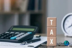Blocks spelling “TAX” next to a calculator and coins, representing Doordash tax deductions.