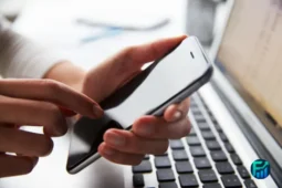 Person using a smartphone next to a laptop, illustrating simplefile by phone for tax filing.