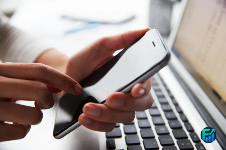 Person using a smartphone next to a laptop, illustrating simplefile by phone for tax filing.
