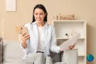 A smiling Canadian woman on a couch viewing a notice of assessment document while checking her Canadian Tax Refund status on her smartphone.
