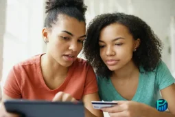 Two women reviewing expenses on a tablet while using their first credit card