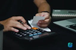Person calculating expenses with a calculator while reviewing bills and personal loans options.